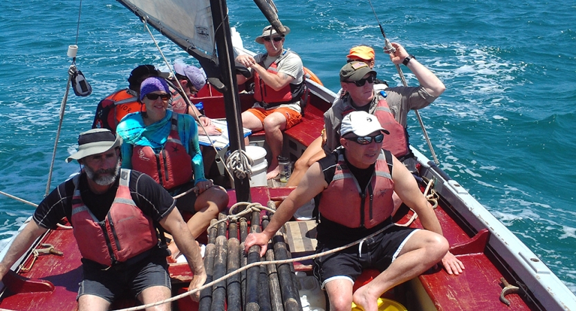 A group of people wearing life jackets sail a boat on blue water. 