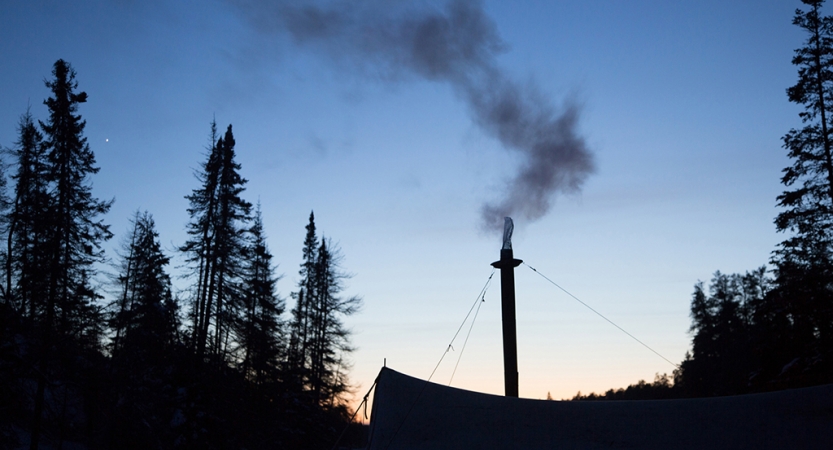 Smoke is emitted from a small chimney coming from a tent at sunset. 